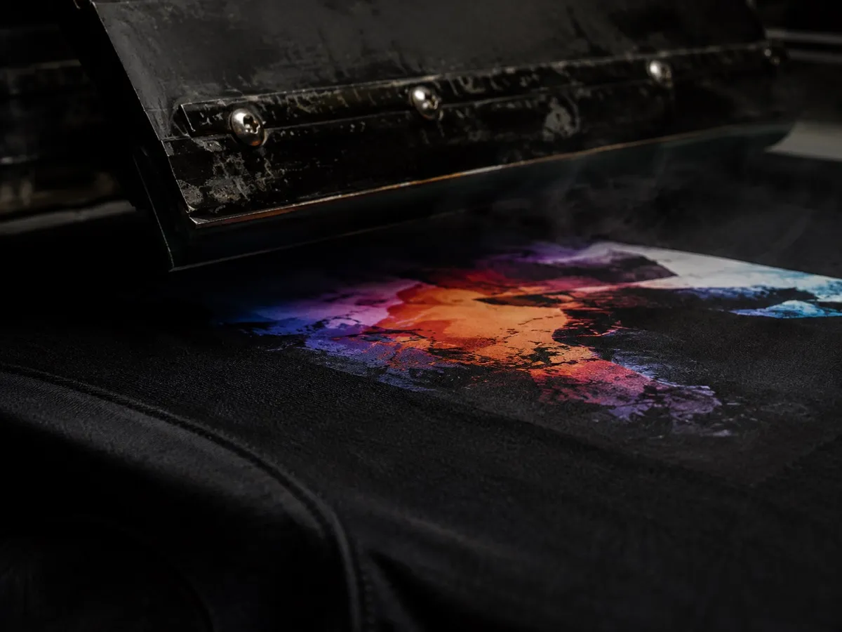 Prensa térmica levantando de uma camiseta preta com transfer DTF colorido recém-aplicado